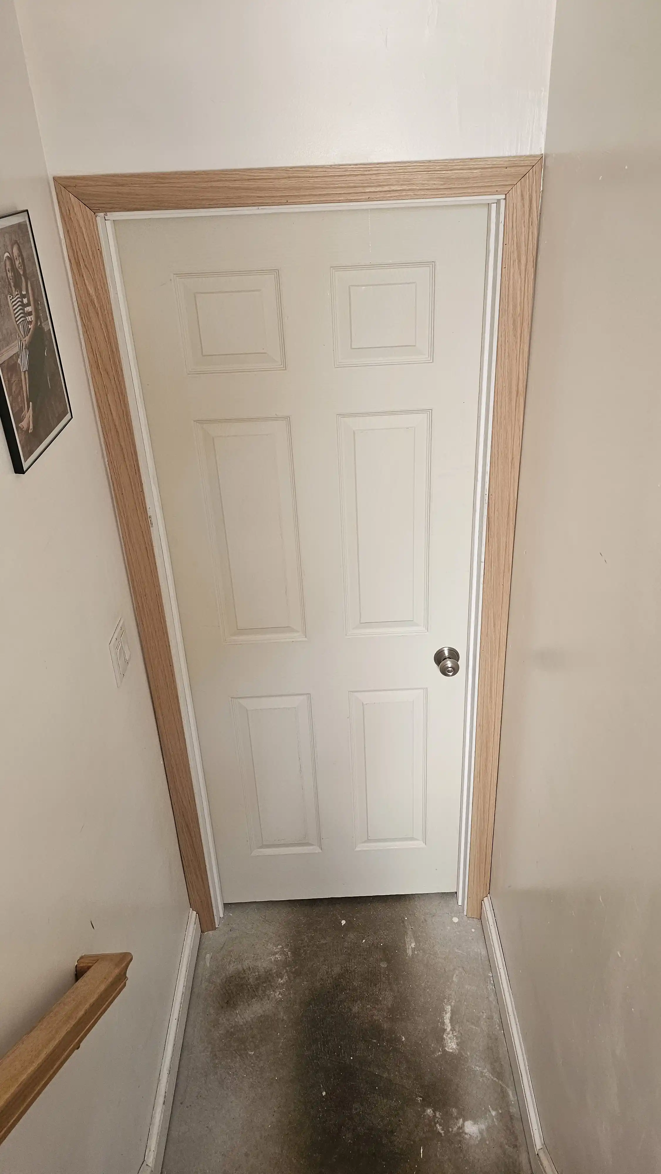 Light wood grain door with six recessed panels and a dark round knob